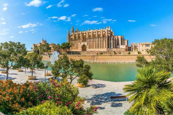 Picture of Catedral-Basílica de Santa María de Mallorca, next to the water, with blue sky and trees in the foreground.