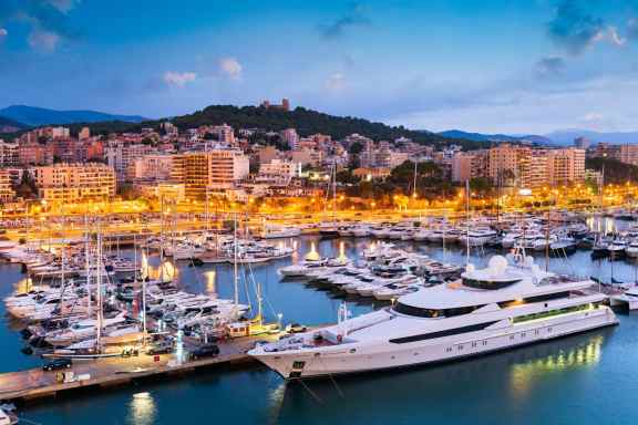 Evening view of the lit up Marina at Palma de Mallorca, with lots of yachts and one huge superyacht in the foreground