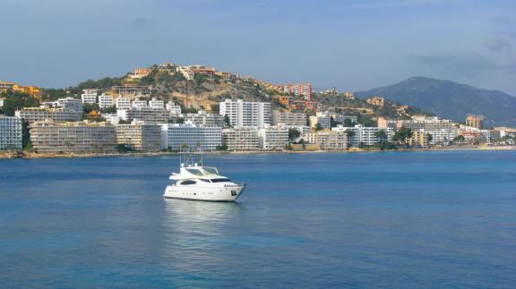 A motor yacht anchored near a coastal city with scenic hills and urban skyline in Mallorca, Spain.